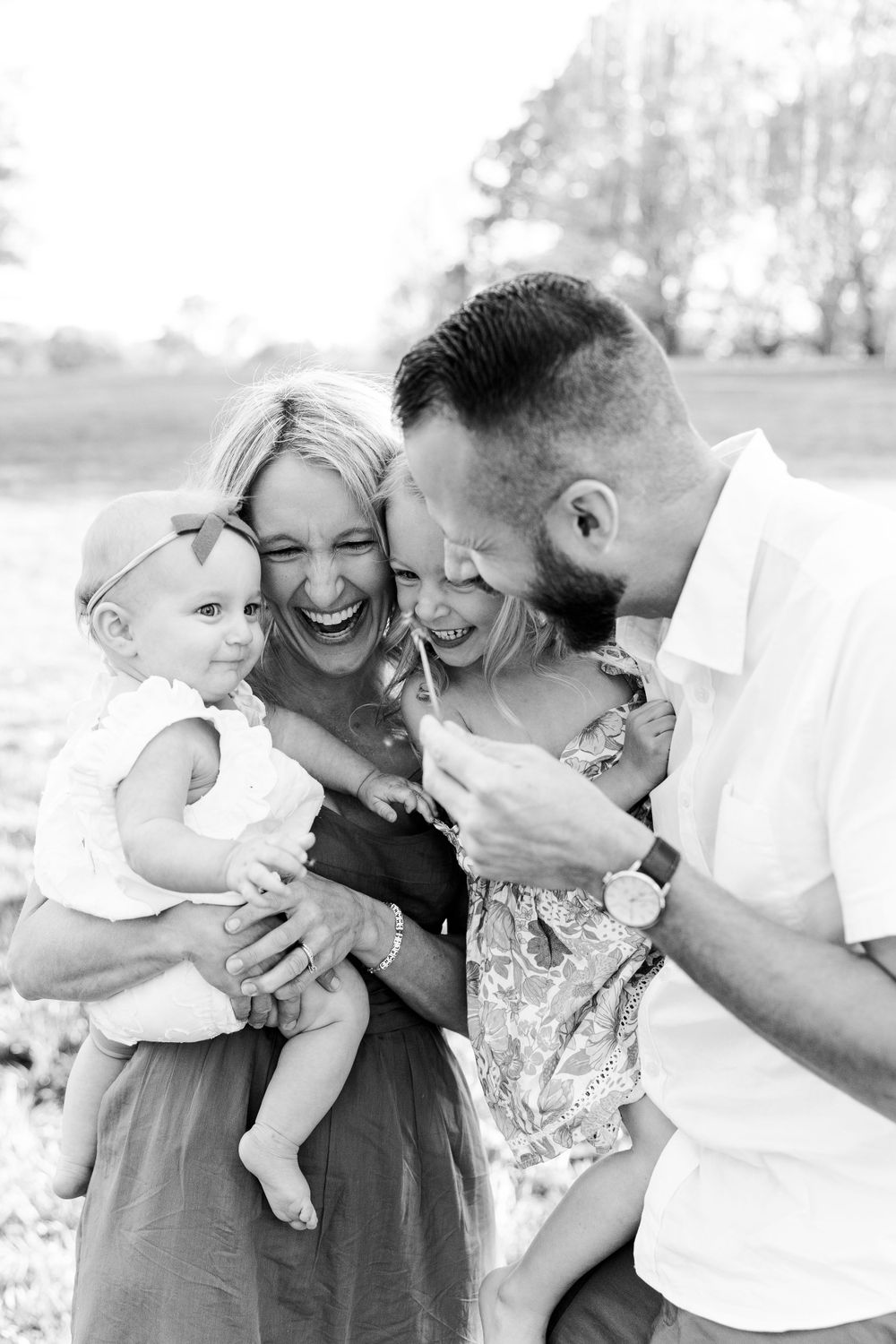 A joyful black and white family portrait captured outdoors showing natural laughter and connection between parents and children.