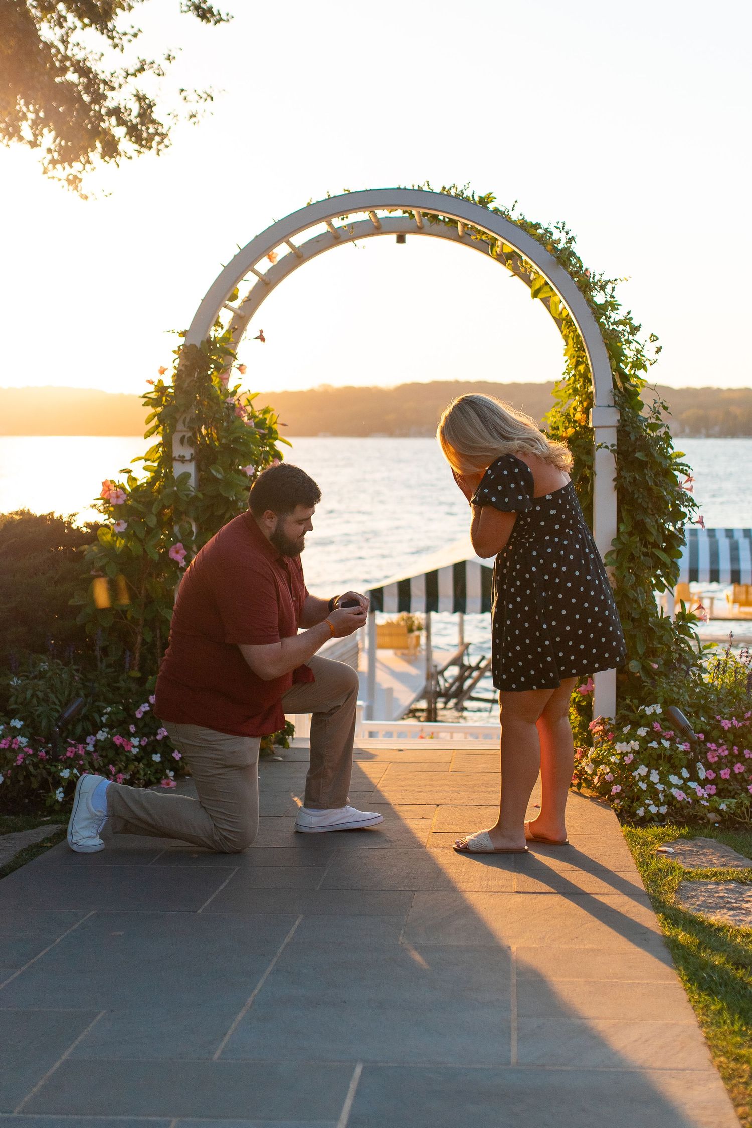 Silhouetted marriage proposal scene under floral arch at sunset by waterfront. Couples photo session. Engagement photo session. Lake Geneva