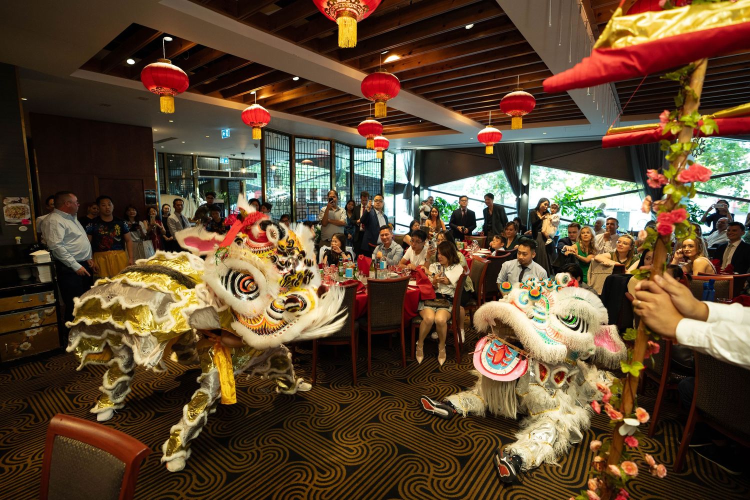 Lion dance performers entertaining guests at an Asian restaurant decorated with red lanterns.