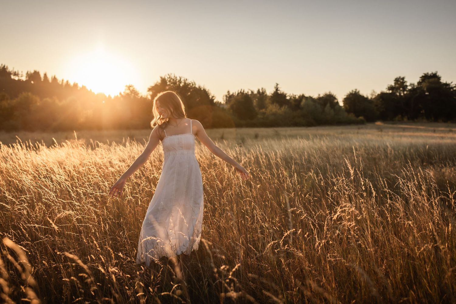 Woman in white dress walking through golden wheat field at stunning sunset.
