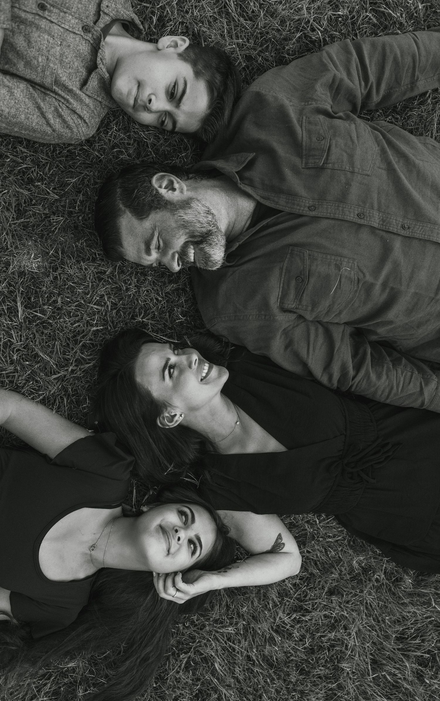 Multi-generational family shares warm embraces and laughter together in black and white portrait outdoors.