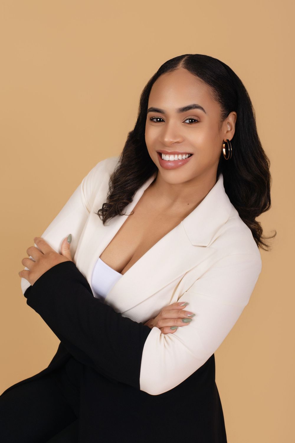 Professional portrait of woman in white blazer and black outfit against beige background.