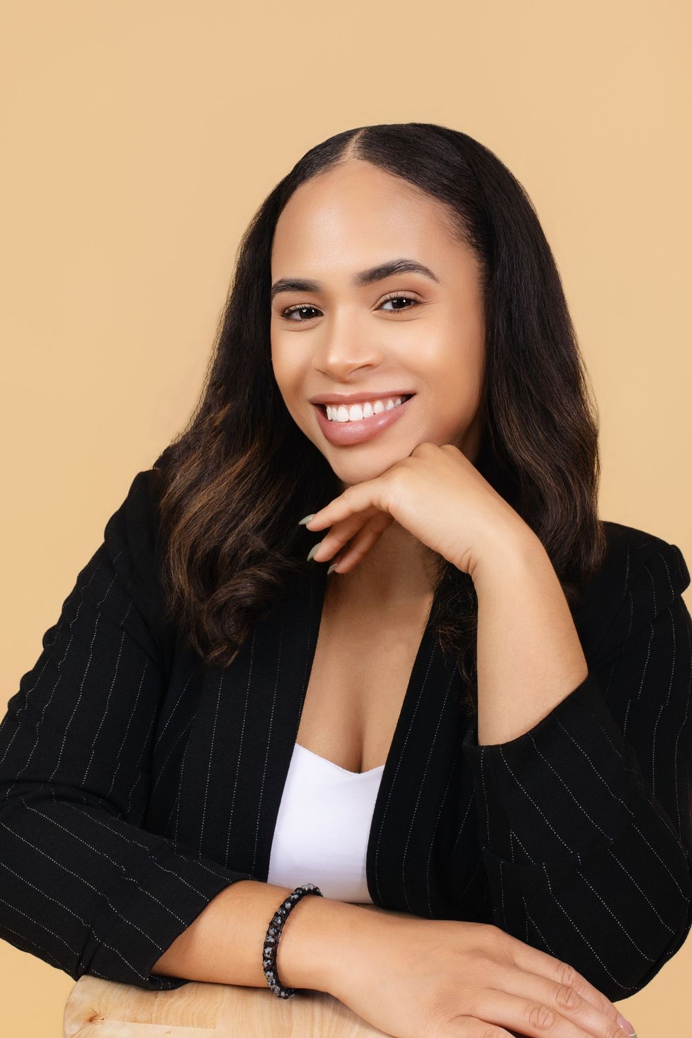 Professional headshot of woman in pinstripe blazer against beige background.
