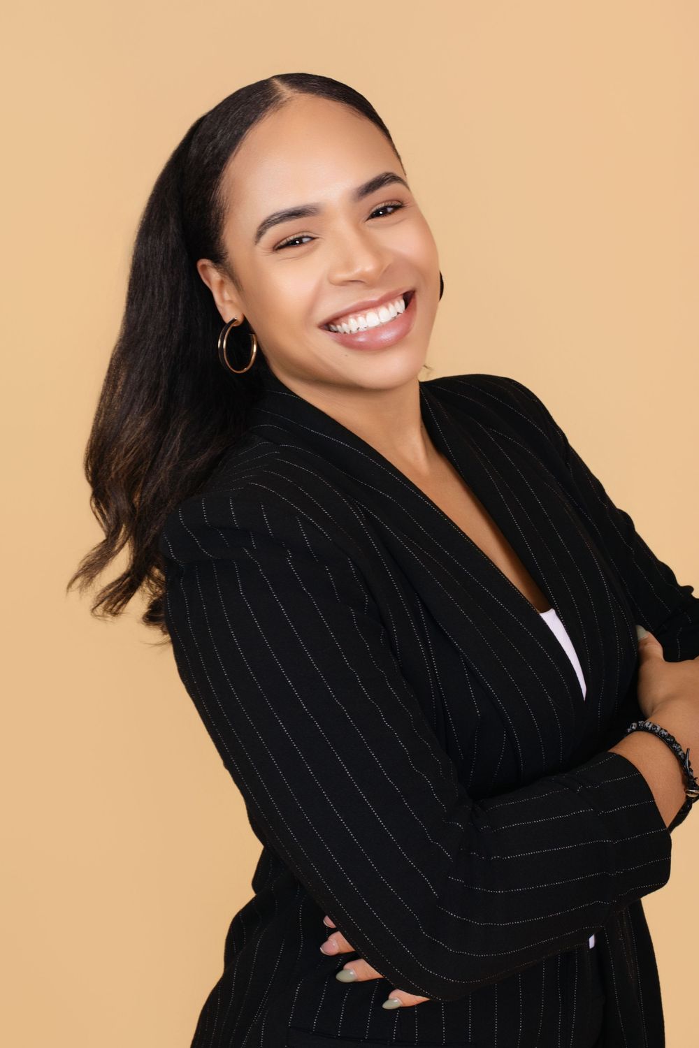 Woman in black blazer smiling warmly against beige background.