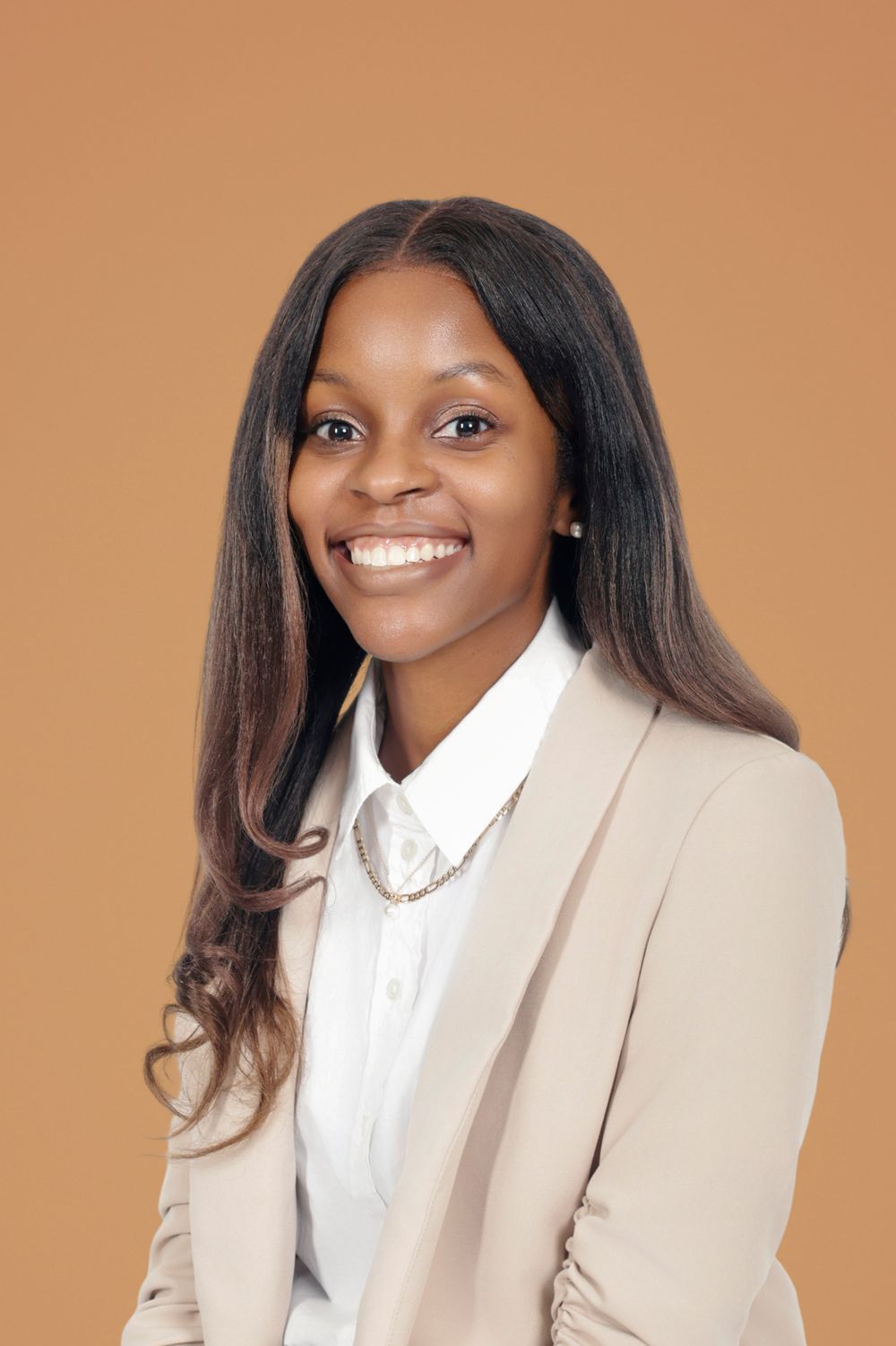Smiling woman in white shirt and beige blazer against orange background.