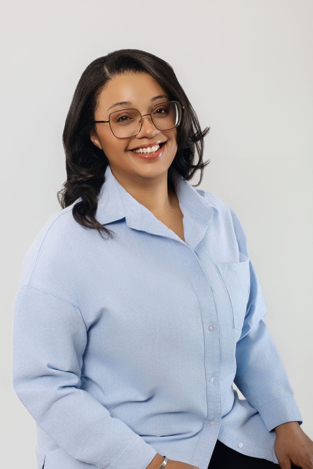 Business professional poses in light blue button-down shirt against white backdrop.