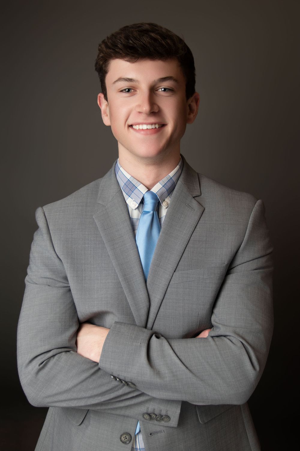 Professional studio portrait in gray suit with blue tie against dark background.