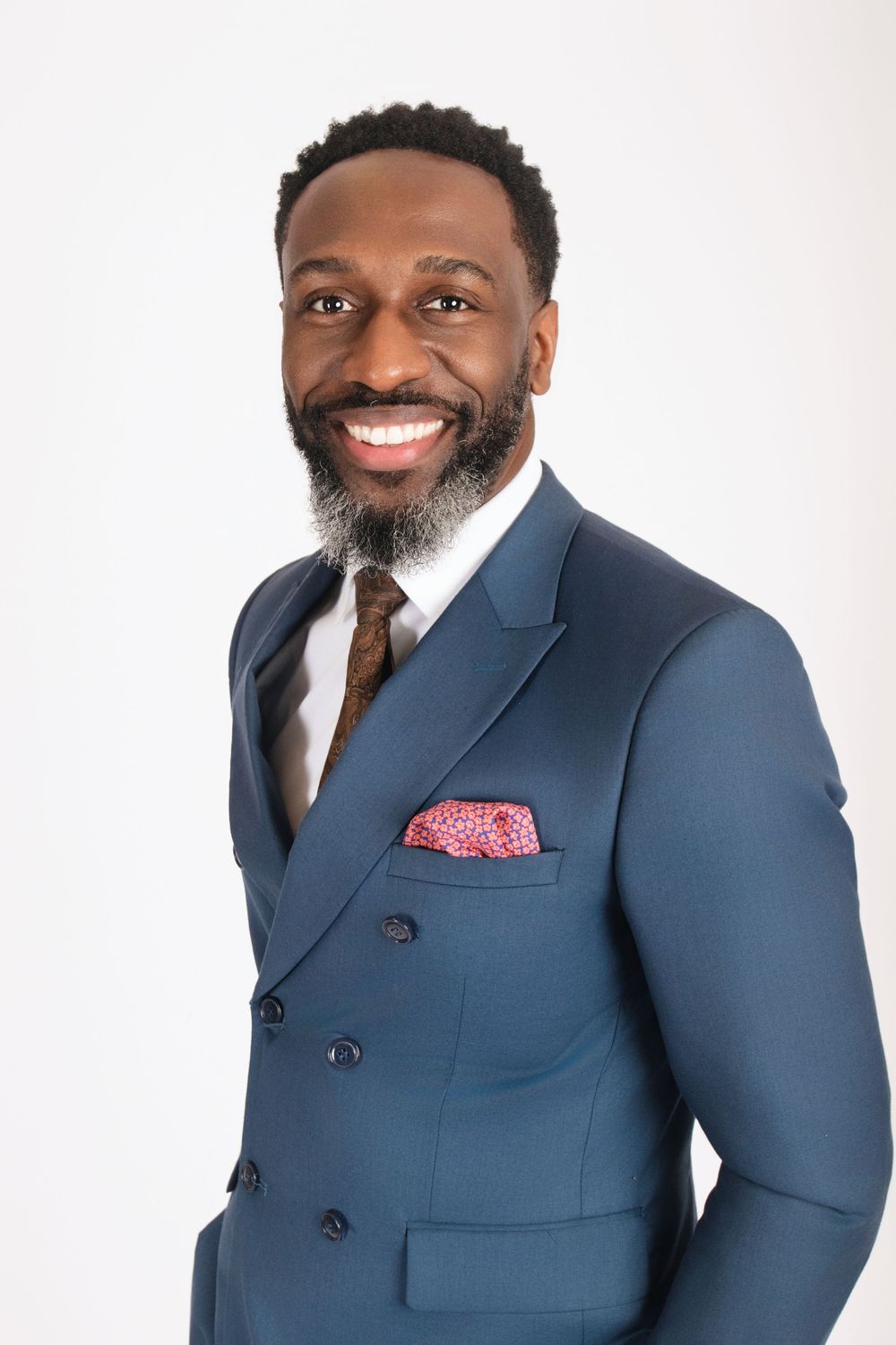 Professional headshot in navy suit with pink pocket square against white background.