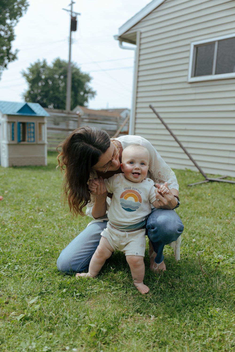 A tender outdoor moment in a backyard with a small child wearing a rainbow t-shirt on a grassy lawn.