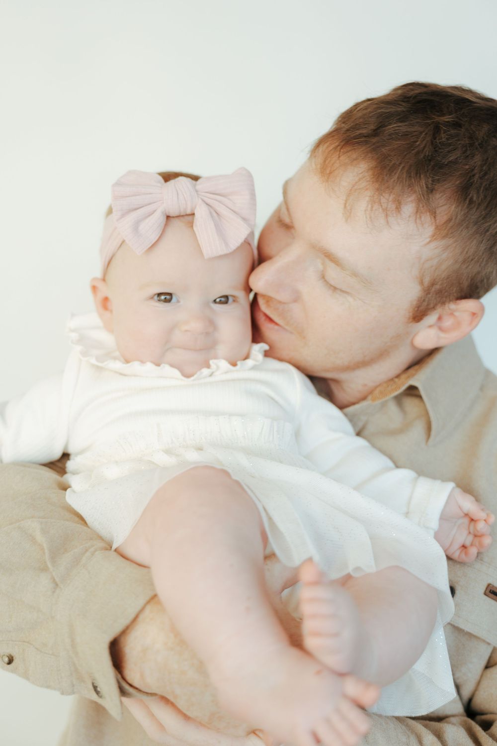 A tender moment between parent and baby in white clothing showing gentle affection and bonding.
