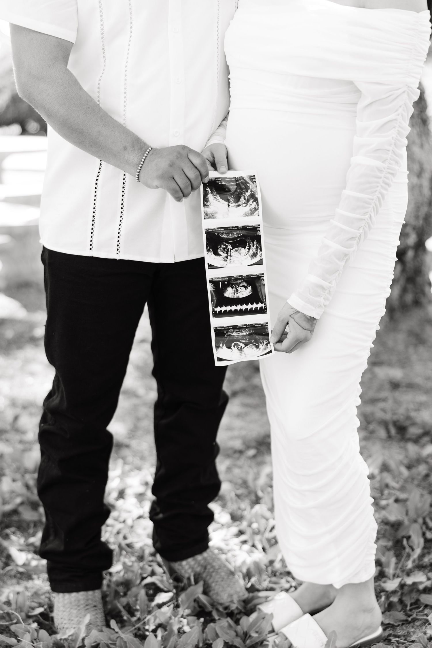 Black and white artistic photo showing legs and feet of people holding ultrasound pictures outdoors.