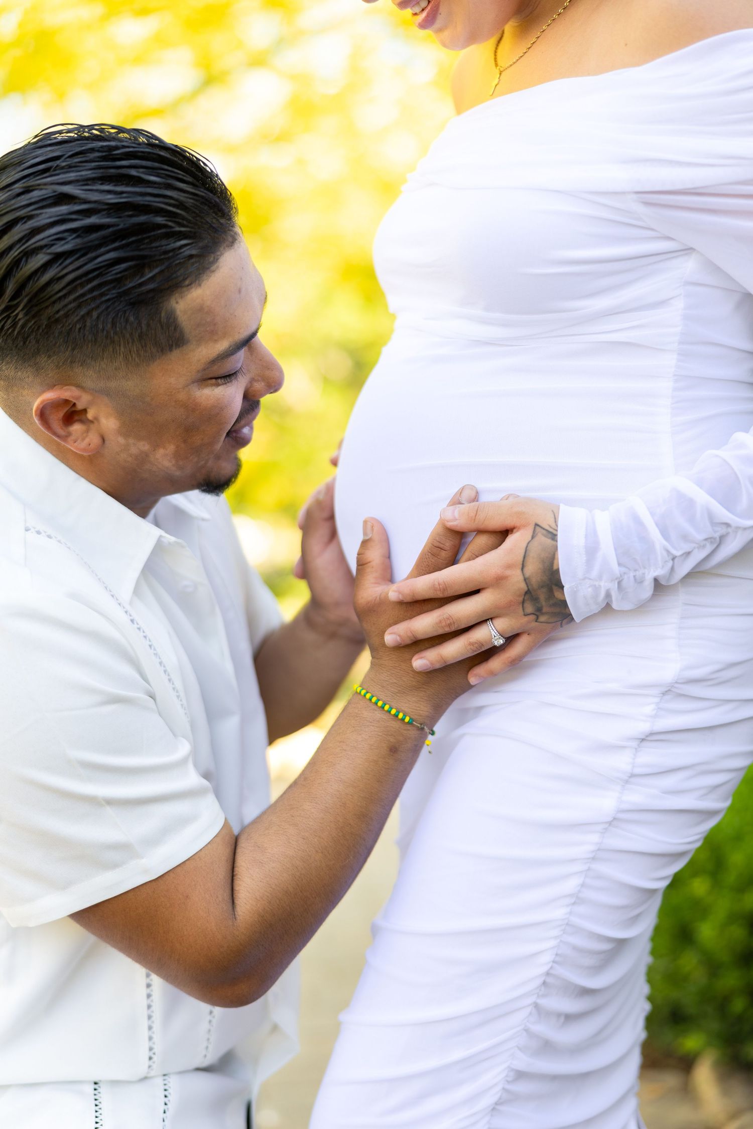 A tender maternity photo with someone in white gently touching a pregnant belly against a warm yellow bokeh background.