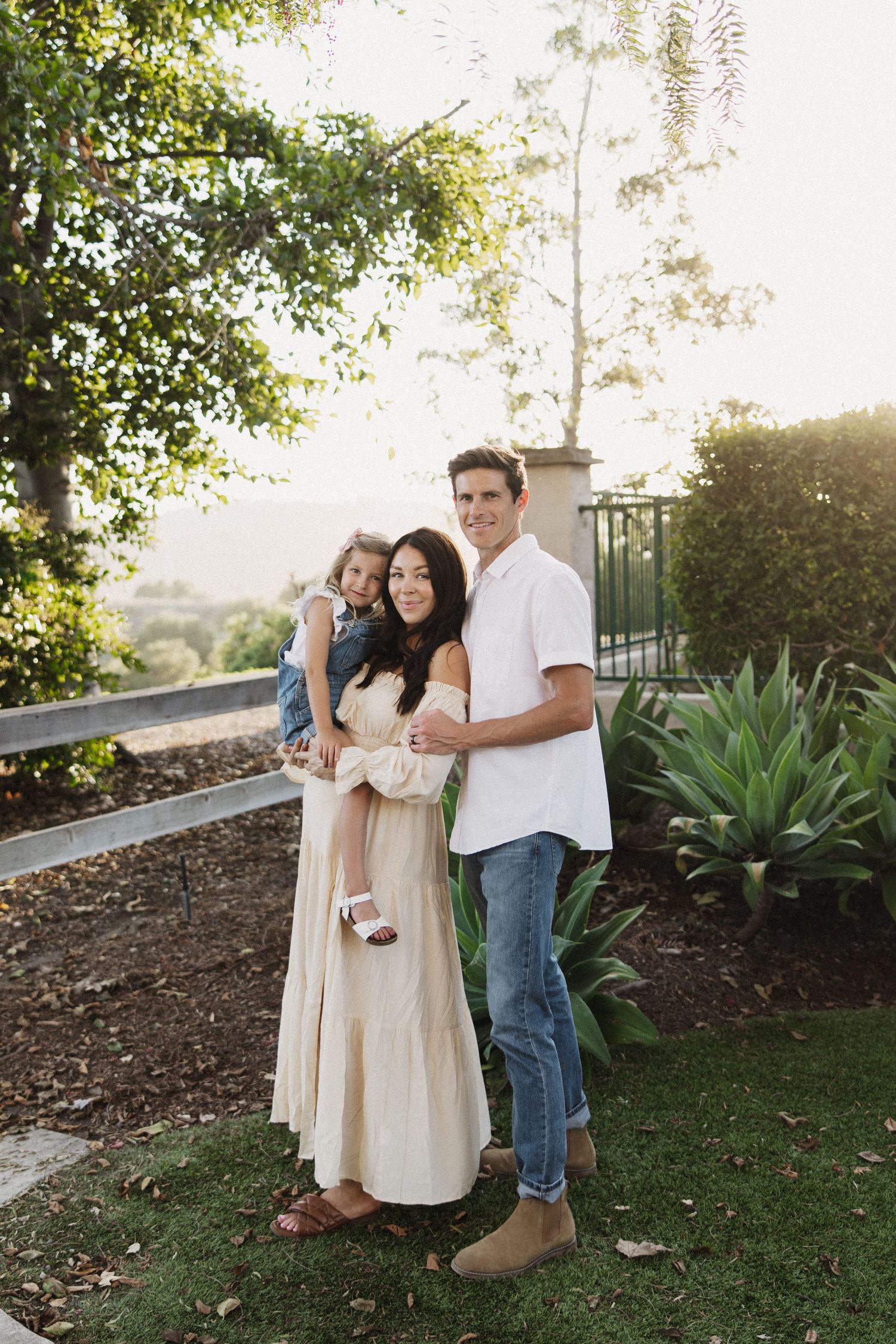 A loving family stands together on a hillside garden at sunset with lush greenery and agave plants in the background.