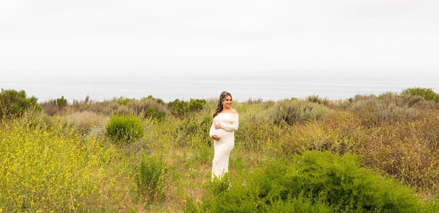 Someone stands in a serene natural setting surrounded by yellow wildflowers and green coastal vegetation on a sunny day.