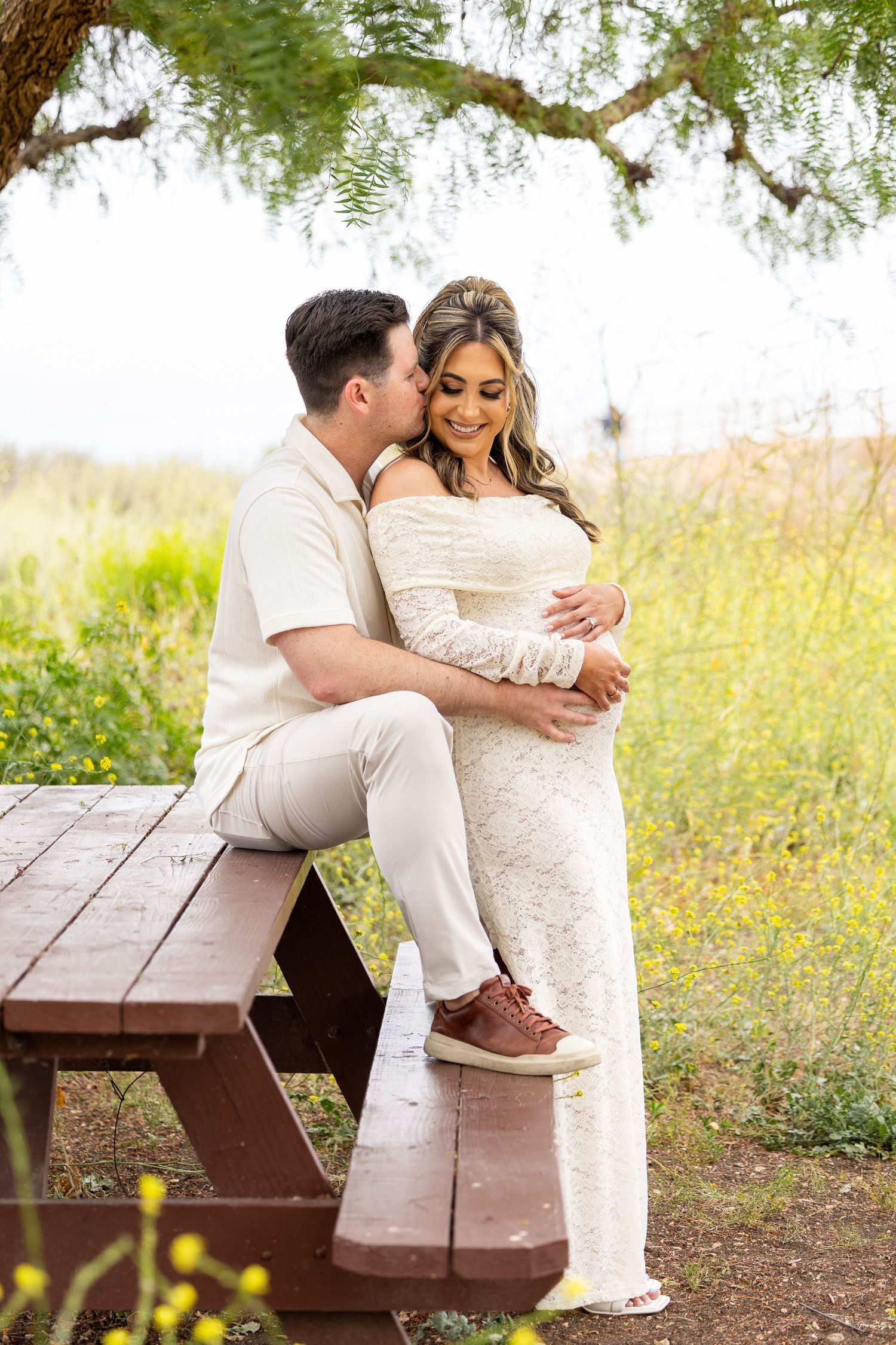 A couple shares intimate moments on a rustic wooden bench surrounded by wildflowers and greenery in nature.