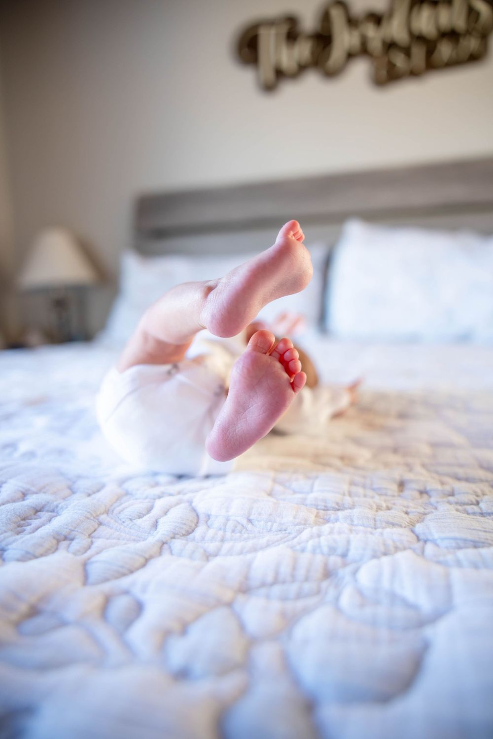 Tiny baby feet with a white quilted bedspread in soft lighting. North Carolina.