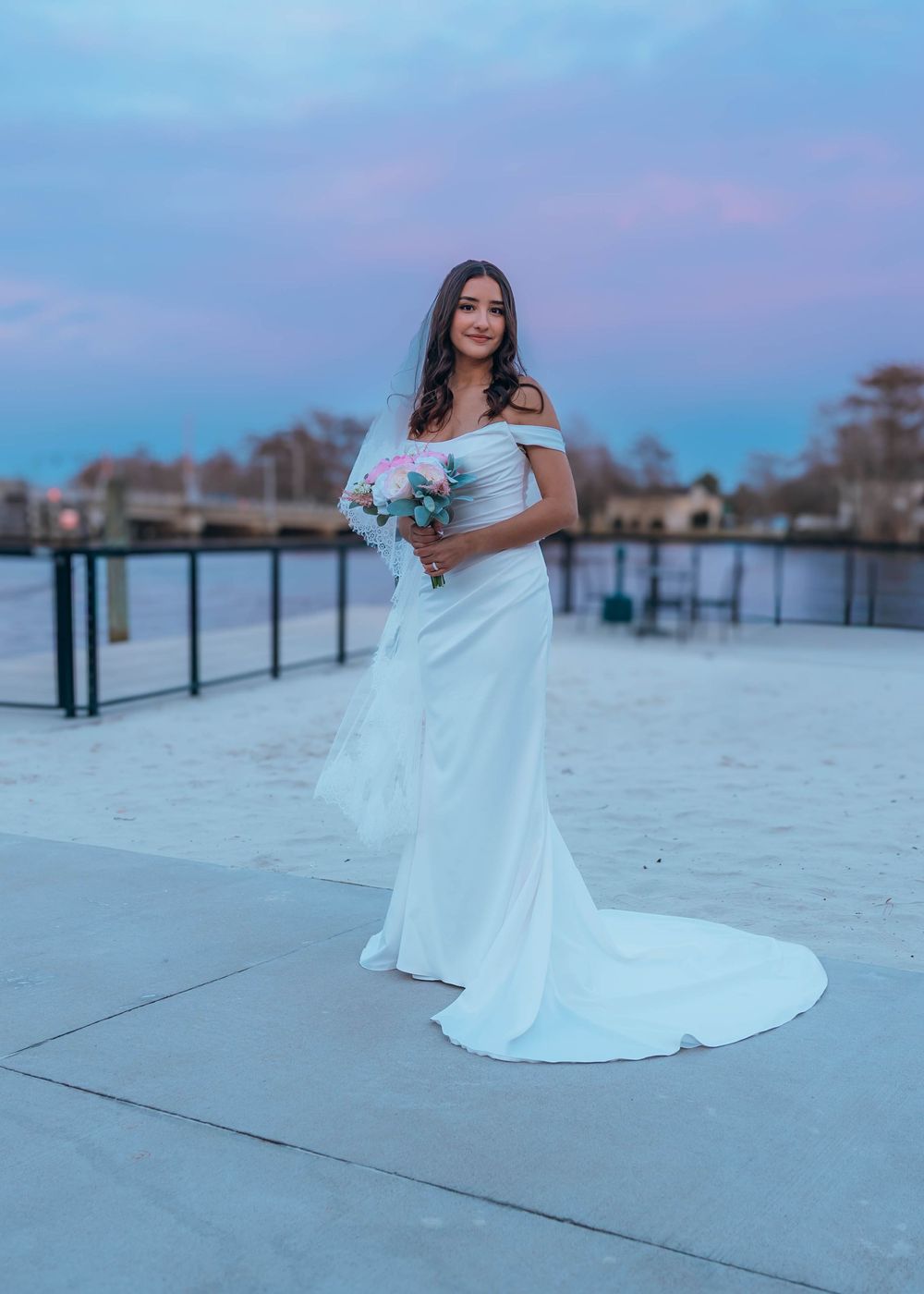 A person in a white wedding dress poses on a sandy beach at dusk with a dreamy pastel sky in the background. North Carolina. OBX.