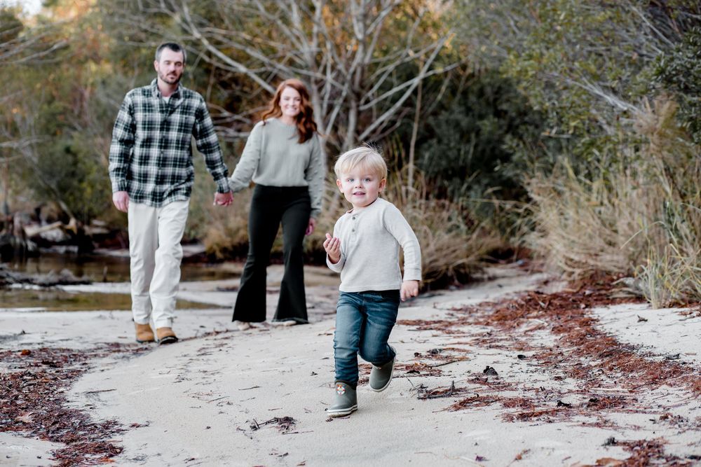 A family walks together on a sandy beach path surrounded by trees and natural vegetation.