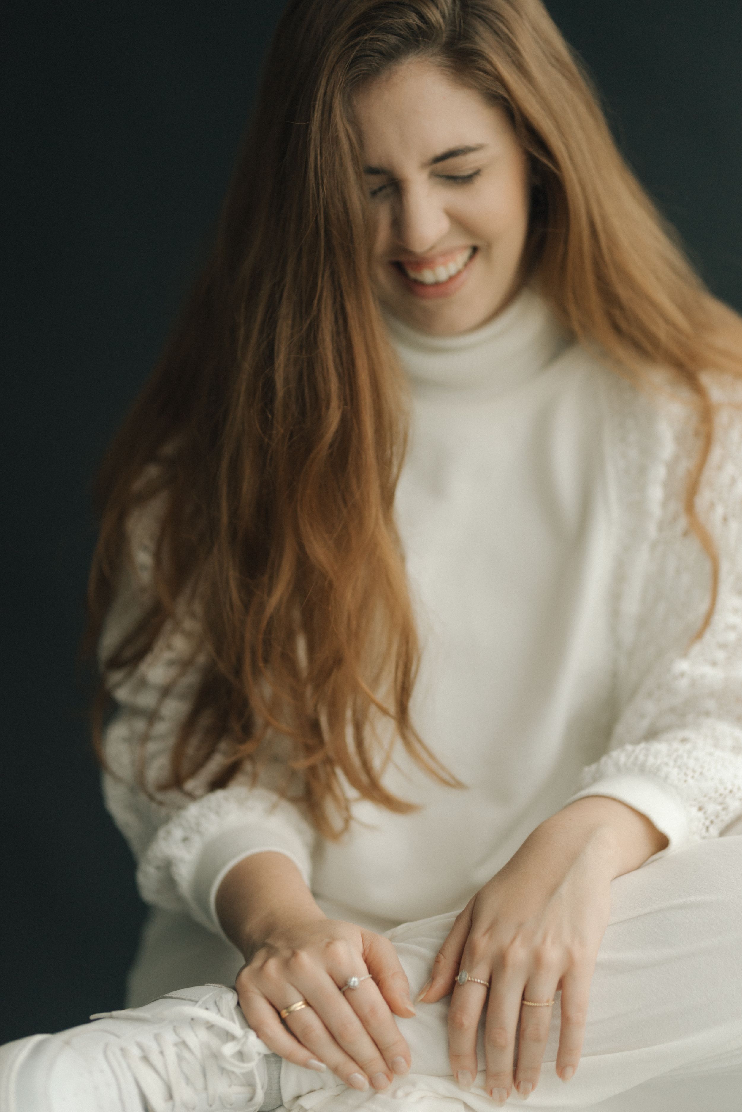 Portrait of a person in a white sweater smiling warmly while looking down at their hands.
