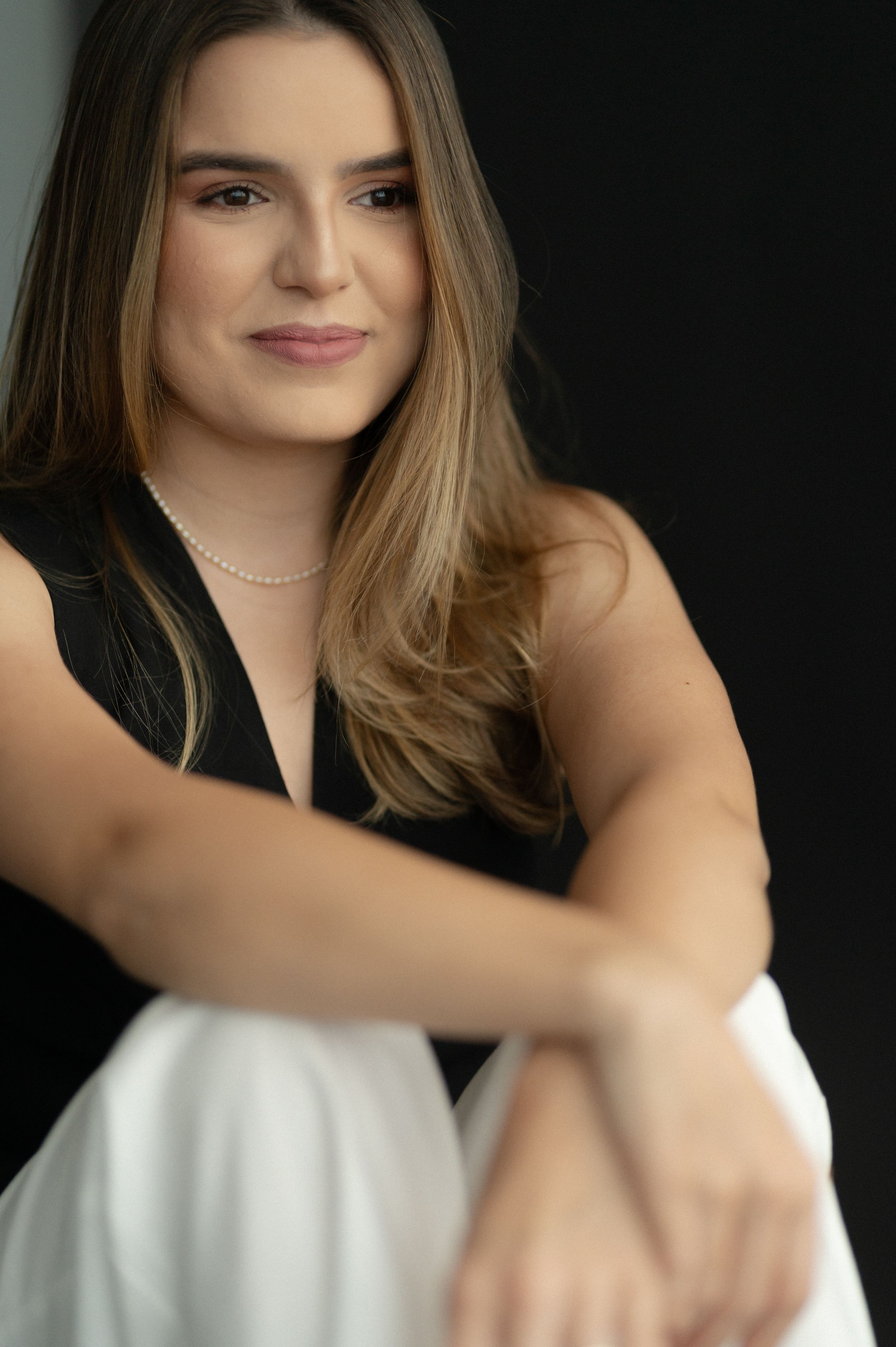 Portrait in a black top and white pants with soft lighting against dark background.