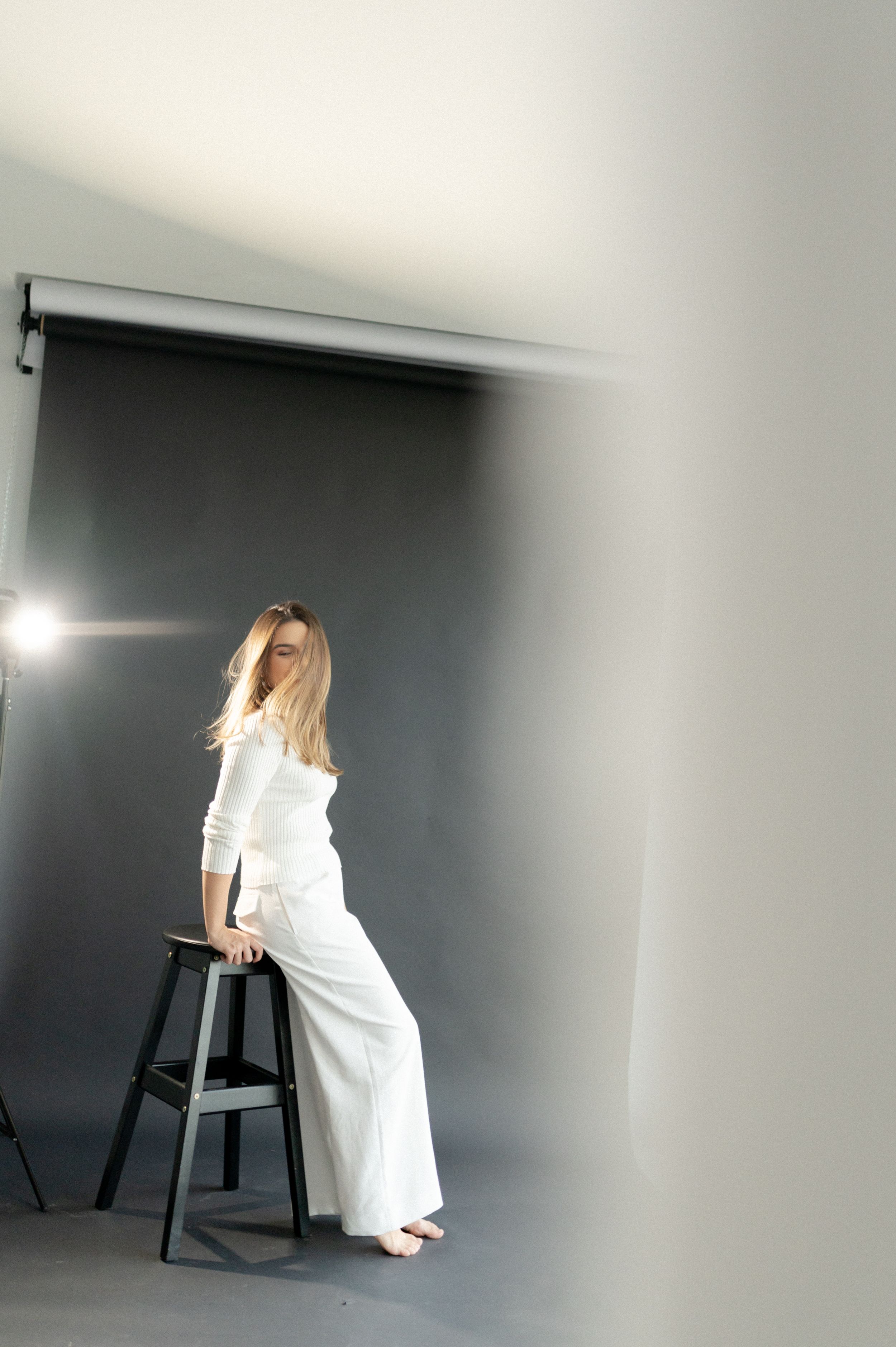 Fashion portrait with white outfit and stool in minimalist studio setting.