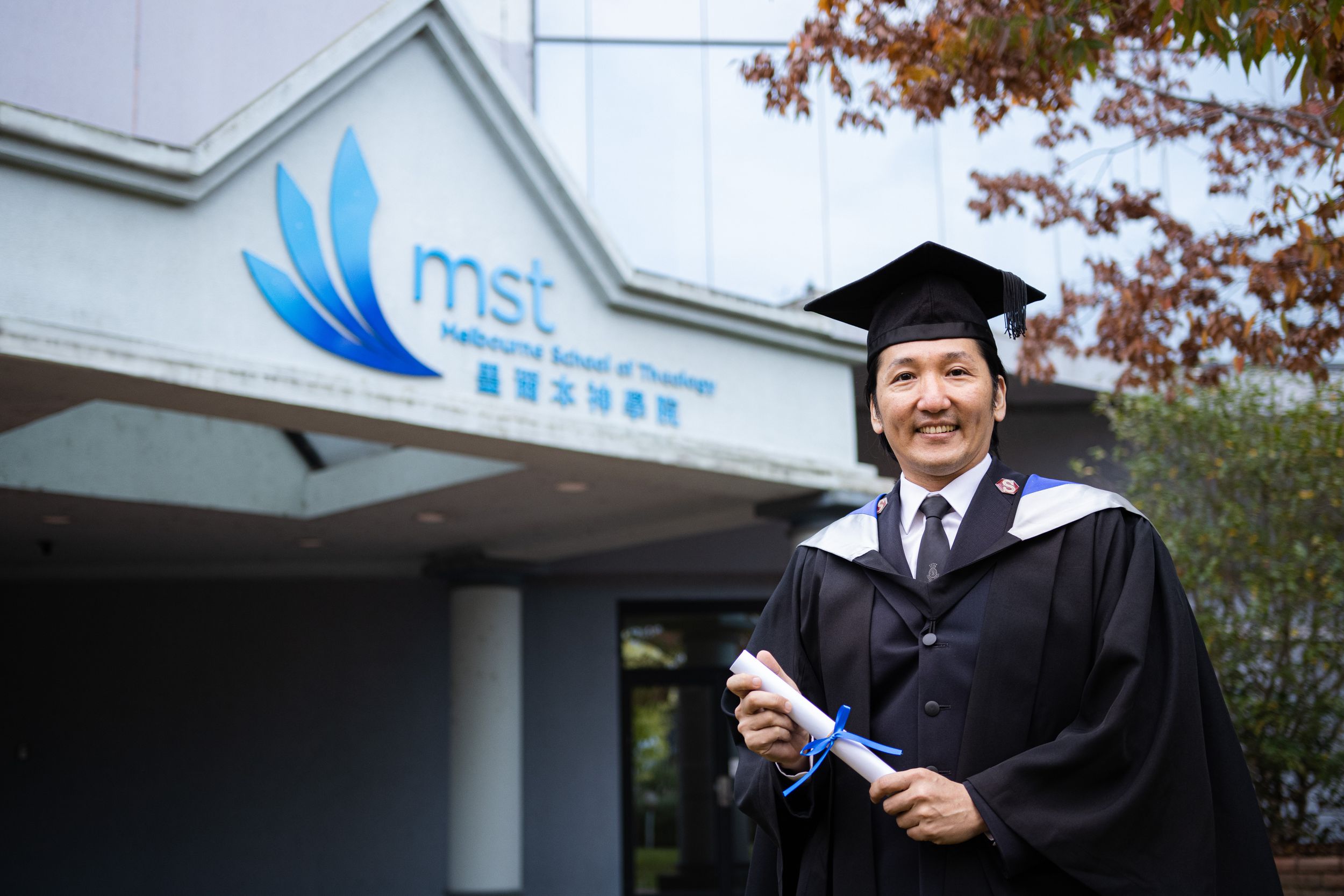 A graduate beams with joy while holding diploma outside MSE building.