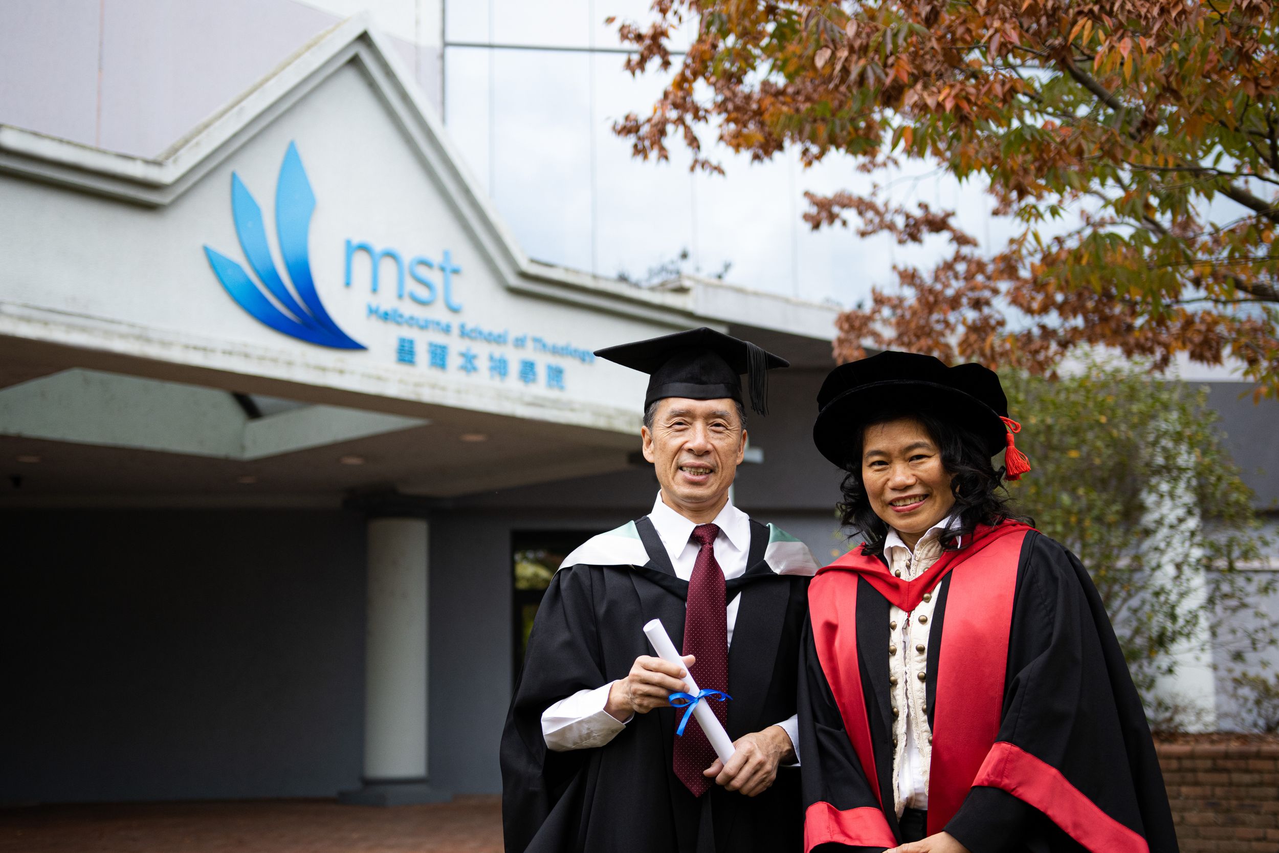 Two graduates in academic regalia celebrate their achievement outside MSE building.