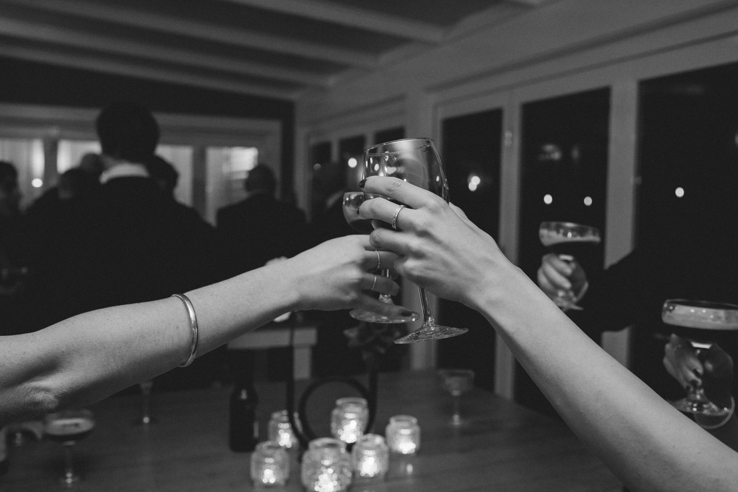 Two hands raise wine glasses in a toast during an evening wedding reception.