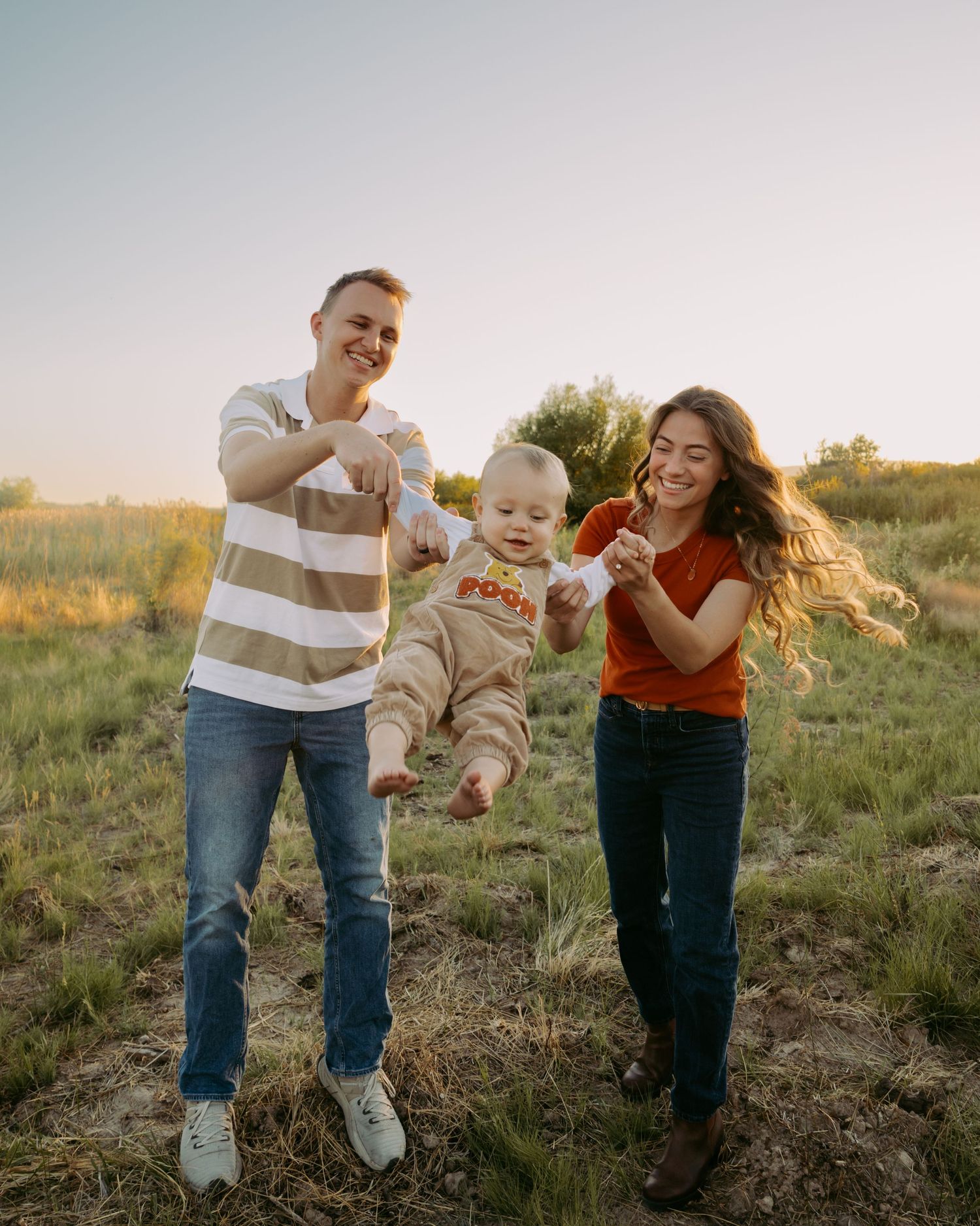 Family playing with toddler in sunlit meadow during golden hour.