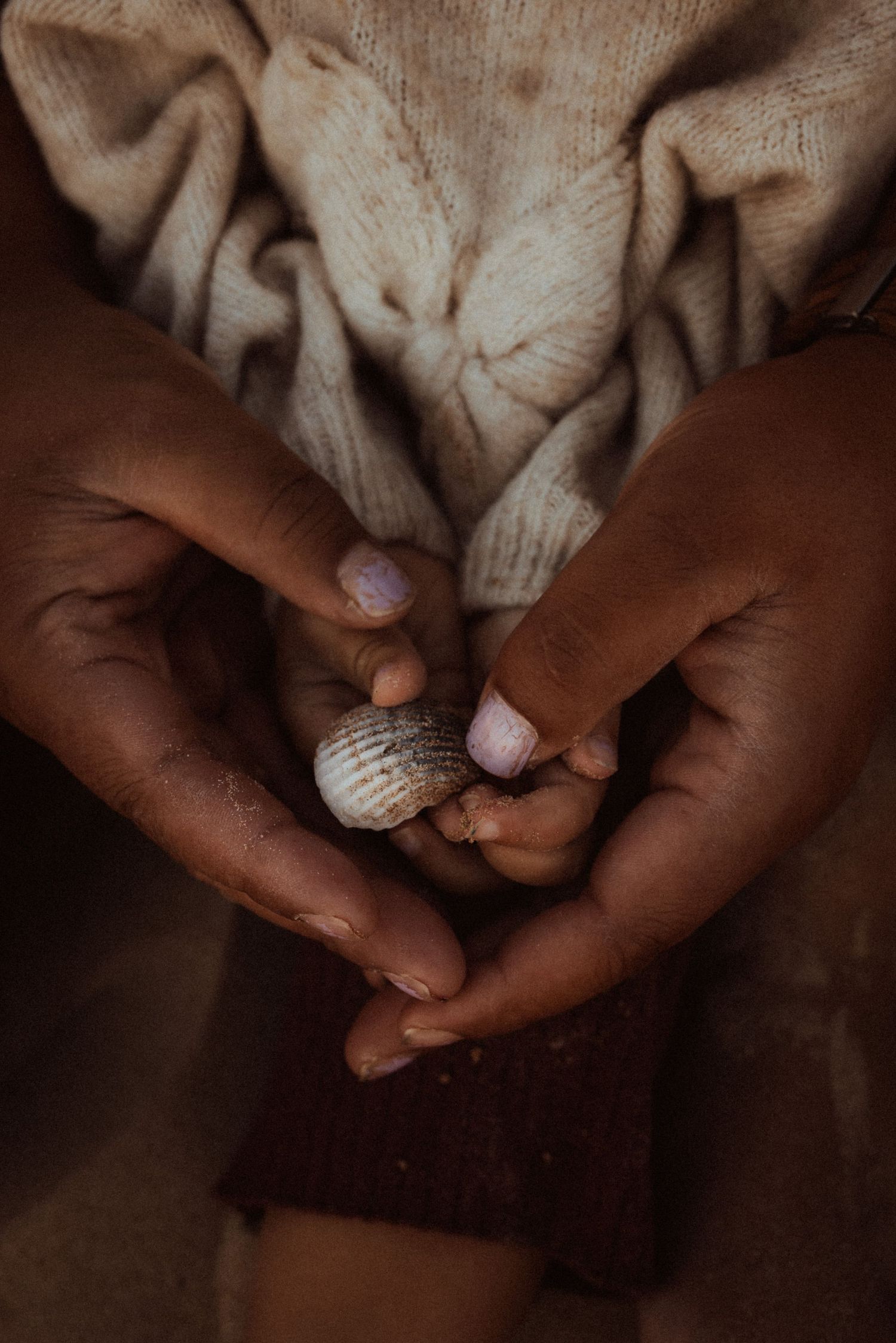 Hands gently holding small seashells in Javea against a soft beige fabric background. Javea photographer