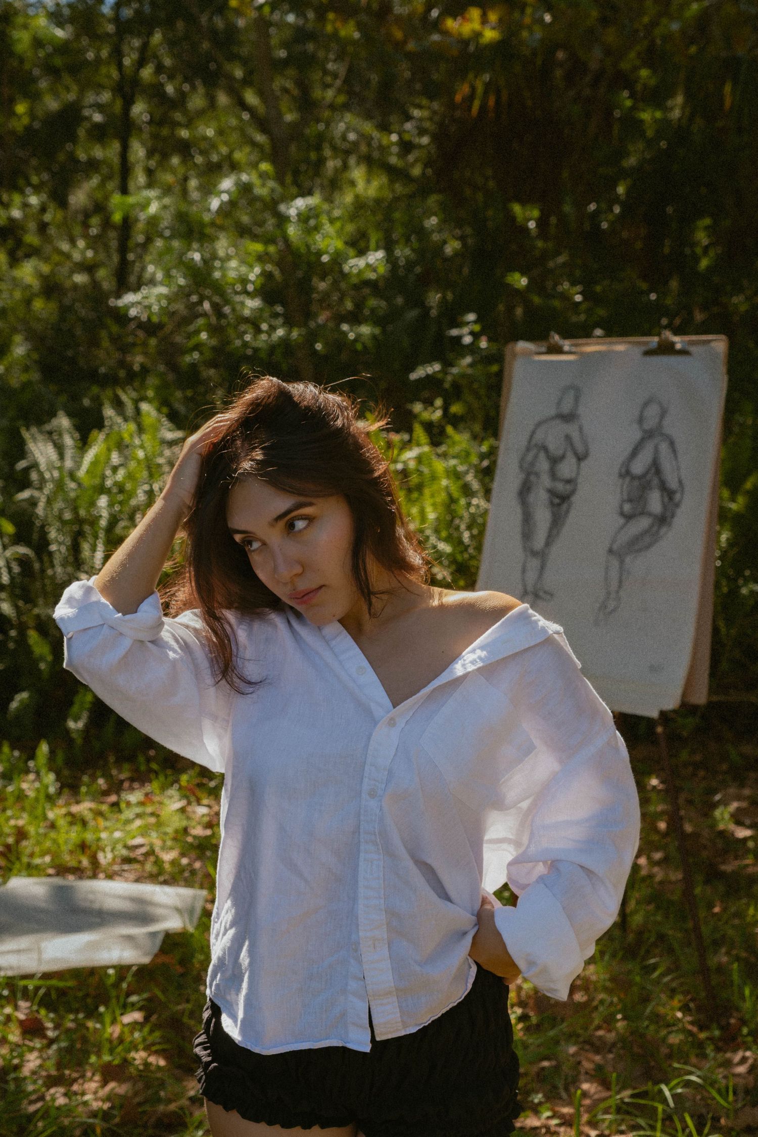A person in a white button-down shirt poses expressively against a natural outdoor backdrop with sketches visible in the scene.