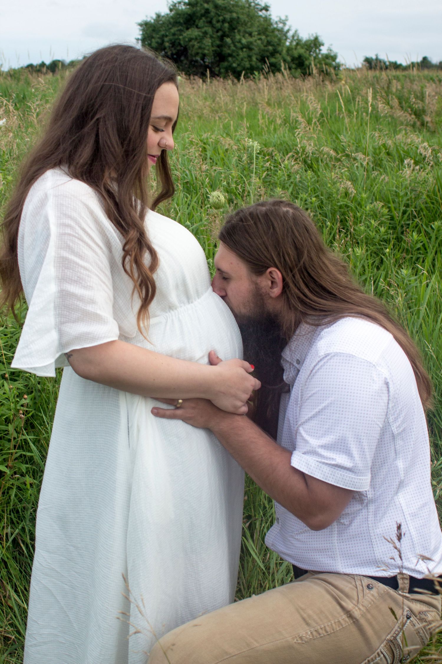 A maternity image where the man is kissing the baby bump and the woman is holding onto the man's hands.