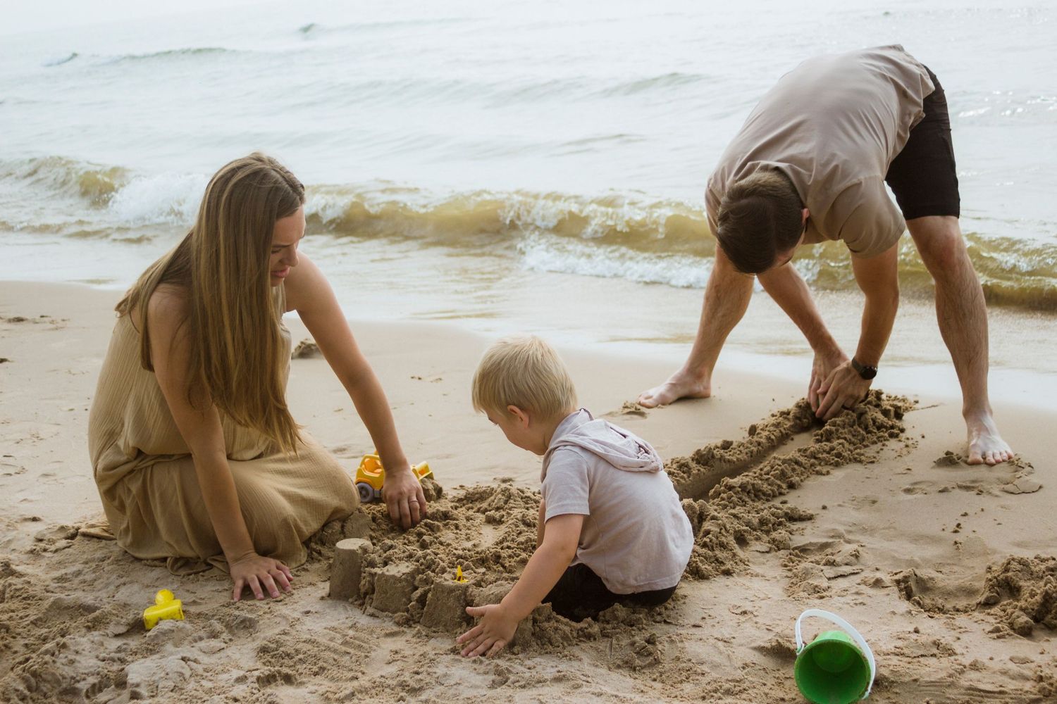 An image of a family of three playing in the sand on a beach.