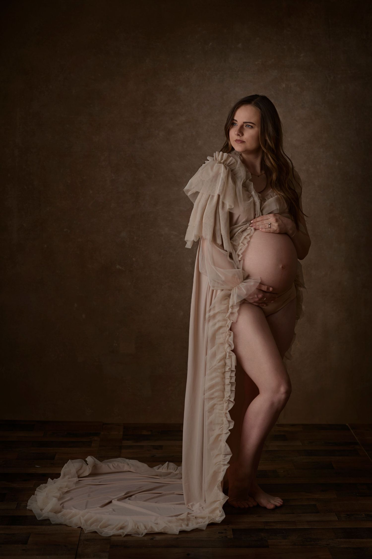 Artistic maternity portrait featuring a flowing beige robe against a dark brown background.  Blackfoot maternity photographer