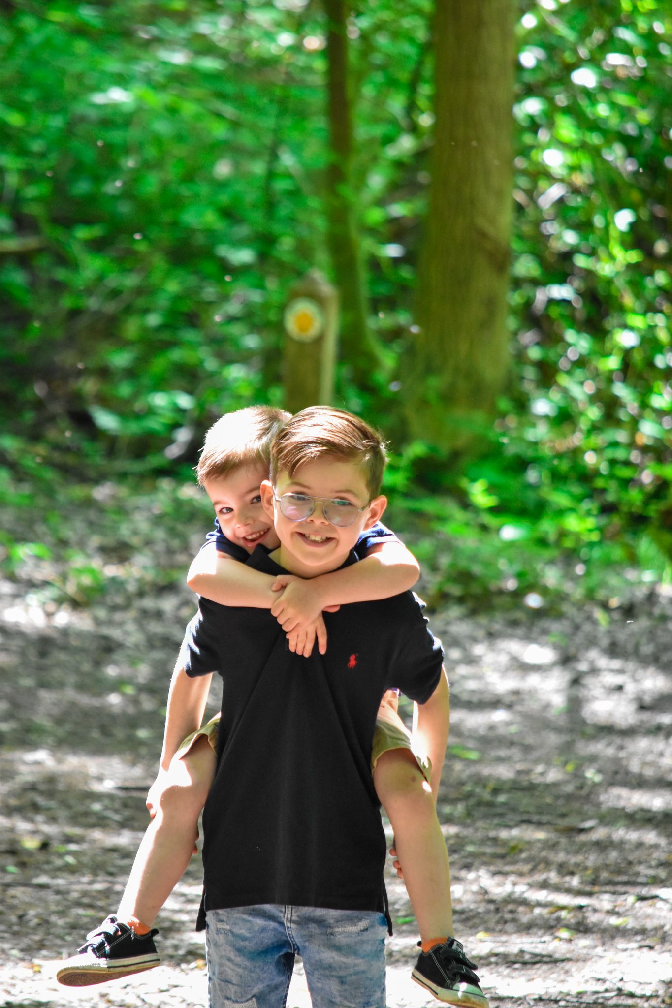 Two boys in black shirts playing piggyback on a forest trail.