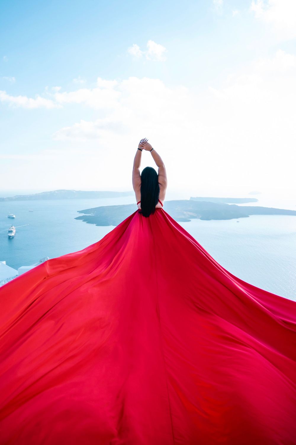 Red flowing dress creates dramatic silhouette against Santorini caldera view.