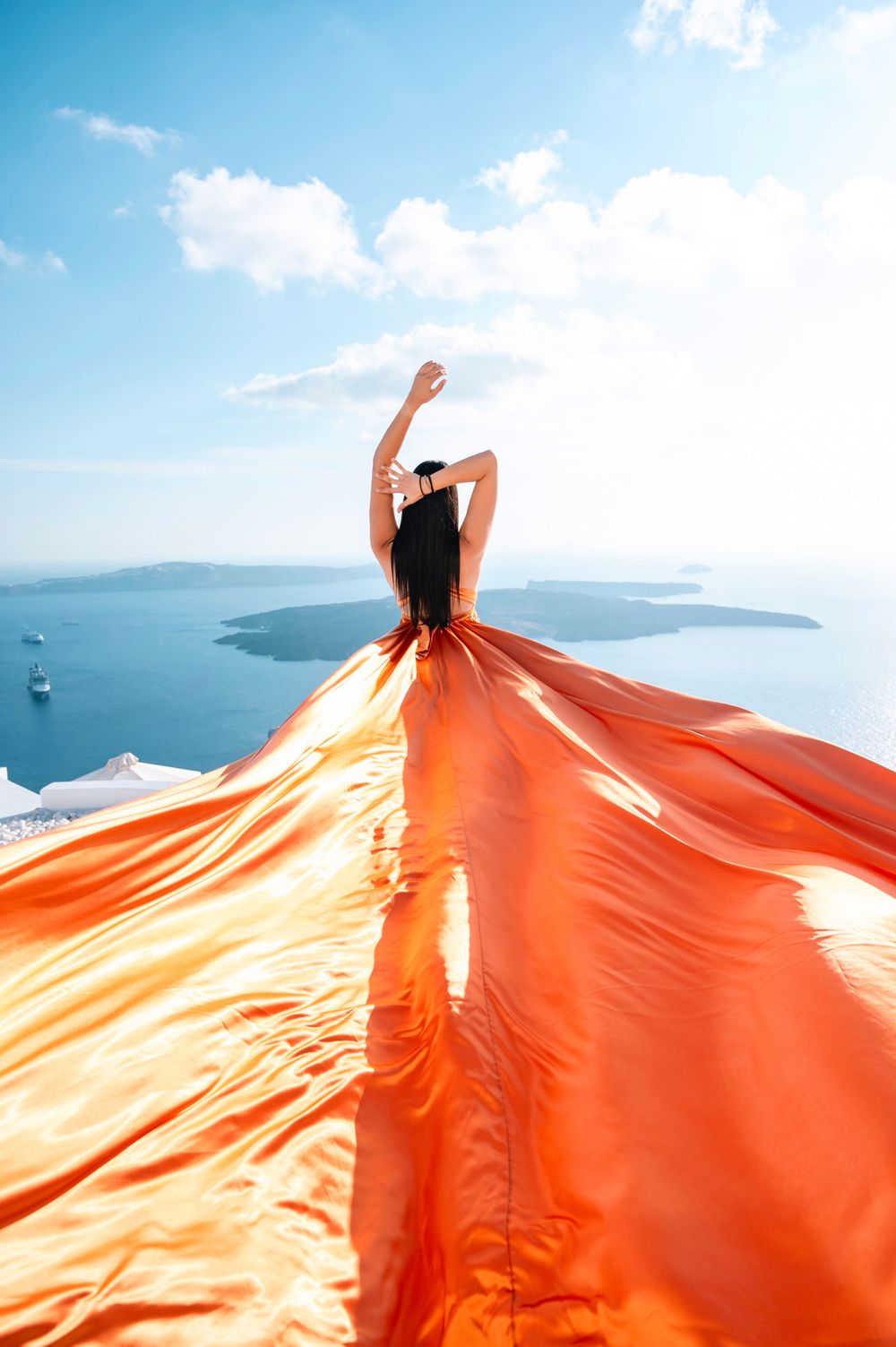 Flowing orange fabric creates dramatic silhouette against Mediterranean sea and sky.