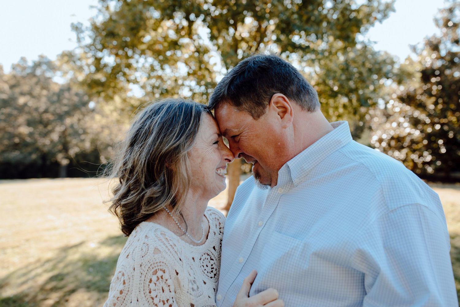 A couple shares an intimate moment while laughing together in warm sunlight.