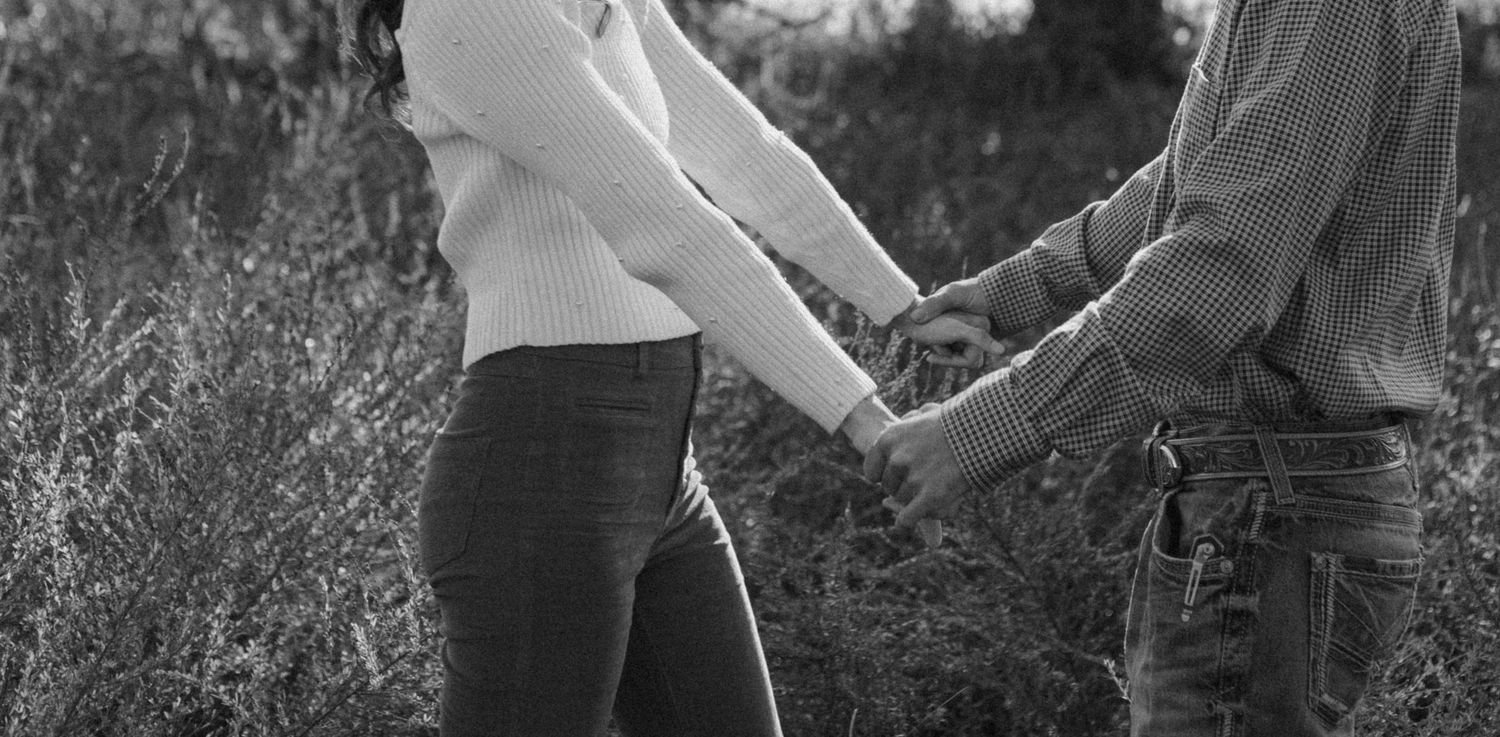 A black and white photo captures two people holding hands in a field.