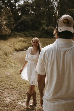 A couple in white clothing walks together through a golden field during a sunny afternoon.