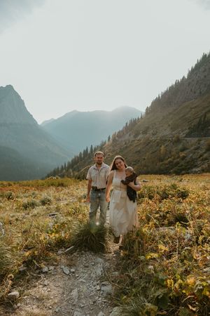 A couple walks hand in hand through a mountain meadow filled with wildflowers on a misty autumn day in Glacier National Park.