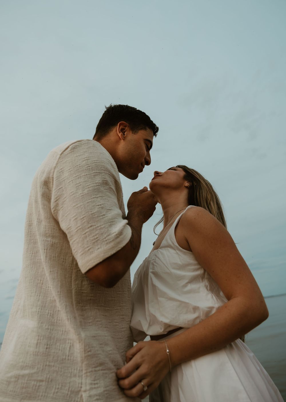 A romantic couple in white and beige outfits share intimate moments in a four-image sequence against a blue background.