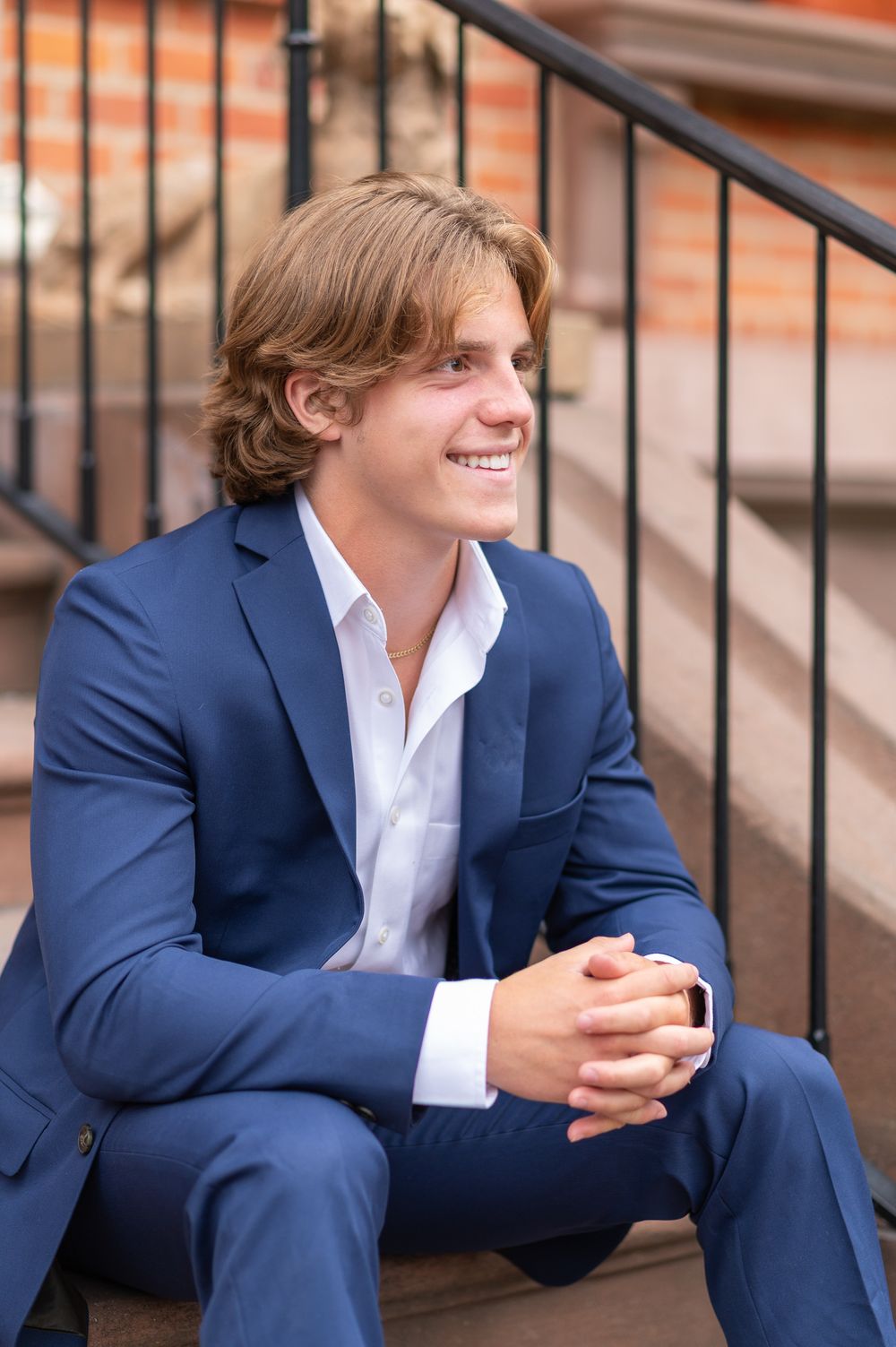 Professional high school senior headshot of a male  in navy suit sitting on outdoor steps