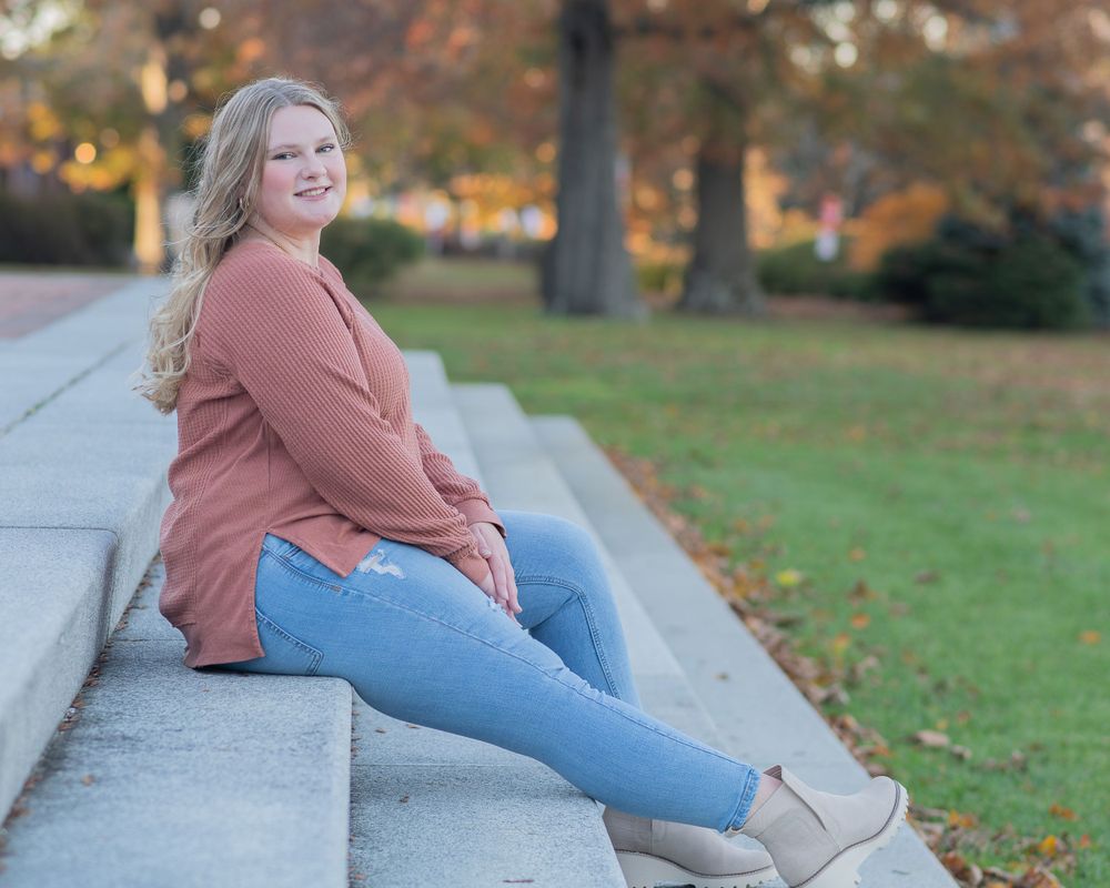 a high school senior in salmon sweater and jeans sitting on concrete steps during autumn