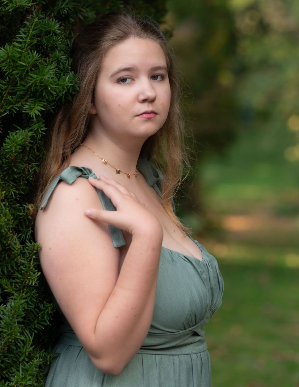 a high school senior wearing A sage green dress with shoulder ties photographed against lush garden greenery