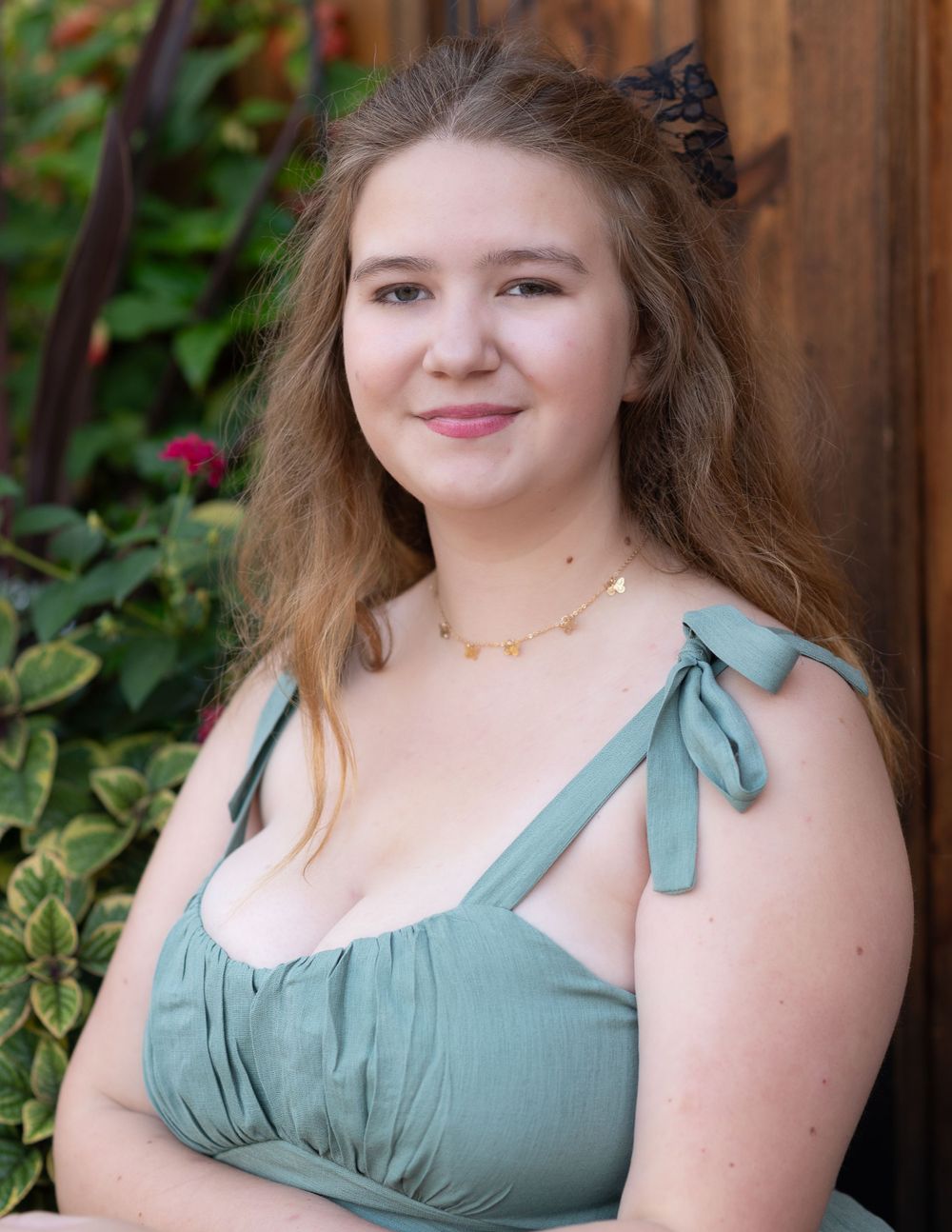 A high school senior in A summery sage green dress with tie straps photographed against a wooden fence and garden