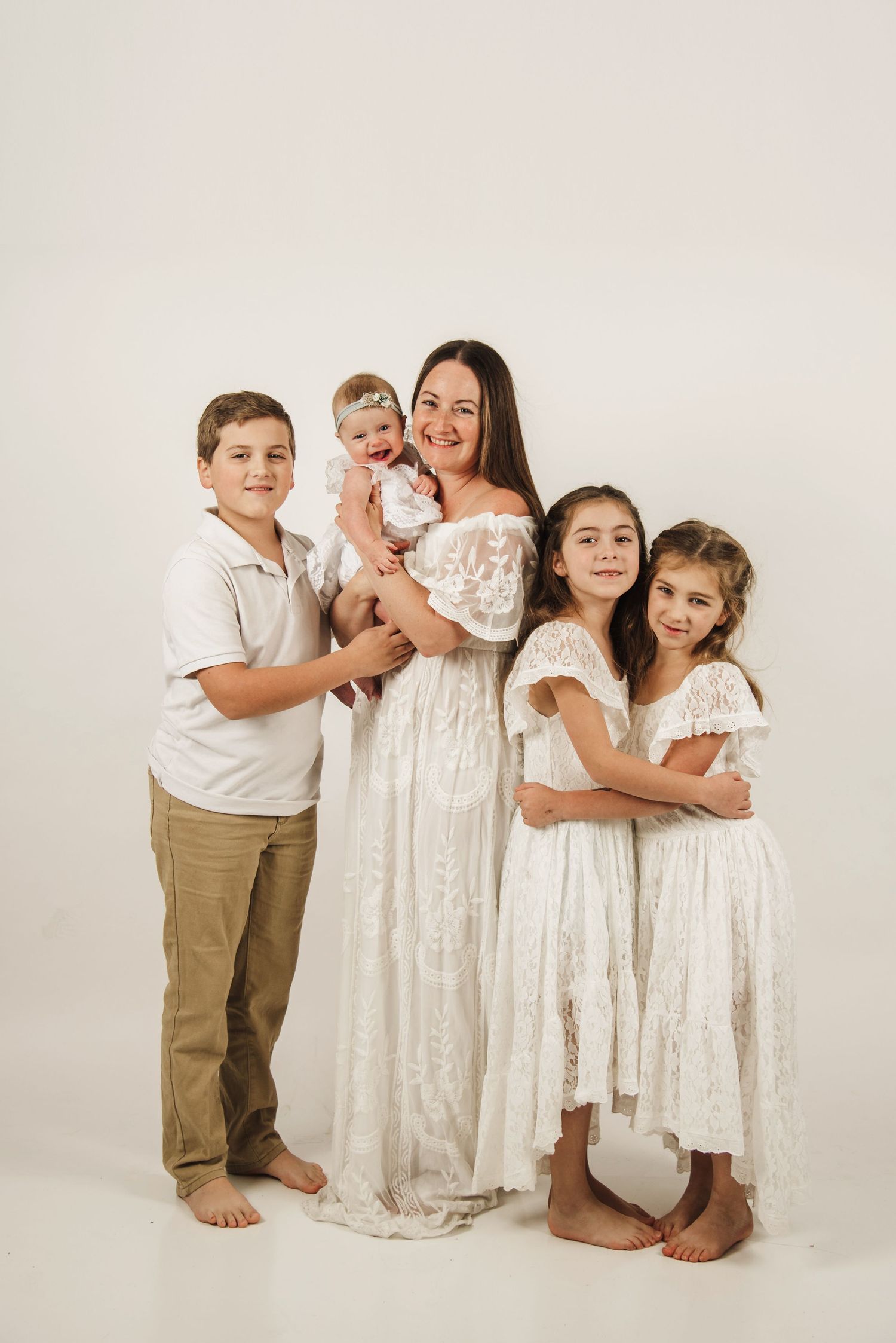 A group in coordinating white and cream outfits pose together on a light studio backdrop.