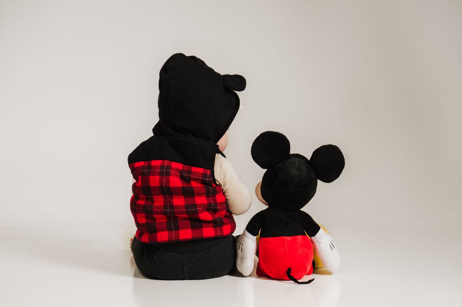 A plush toy wearing buffalo plaid sits next to a Mickey Mouse stuffed animal against a neutral backdrop.