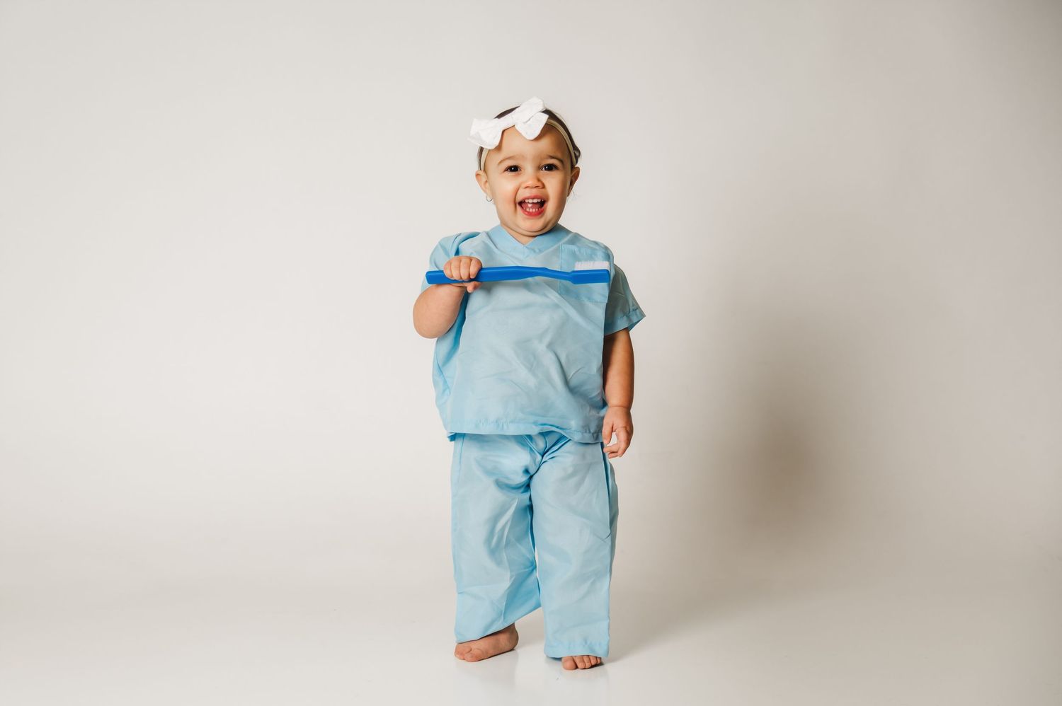 A series of four photos showing a toddler in light blue scrubs and a white cap posing playfully against a neutral background.