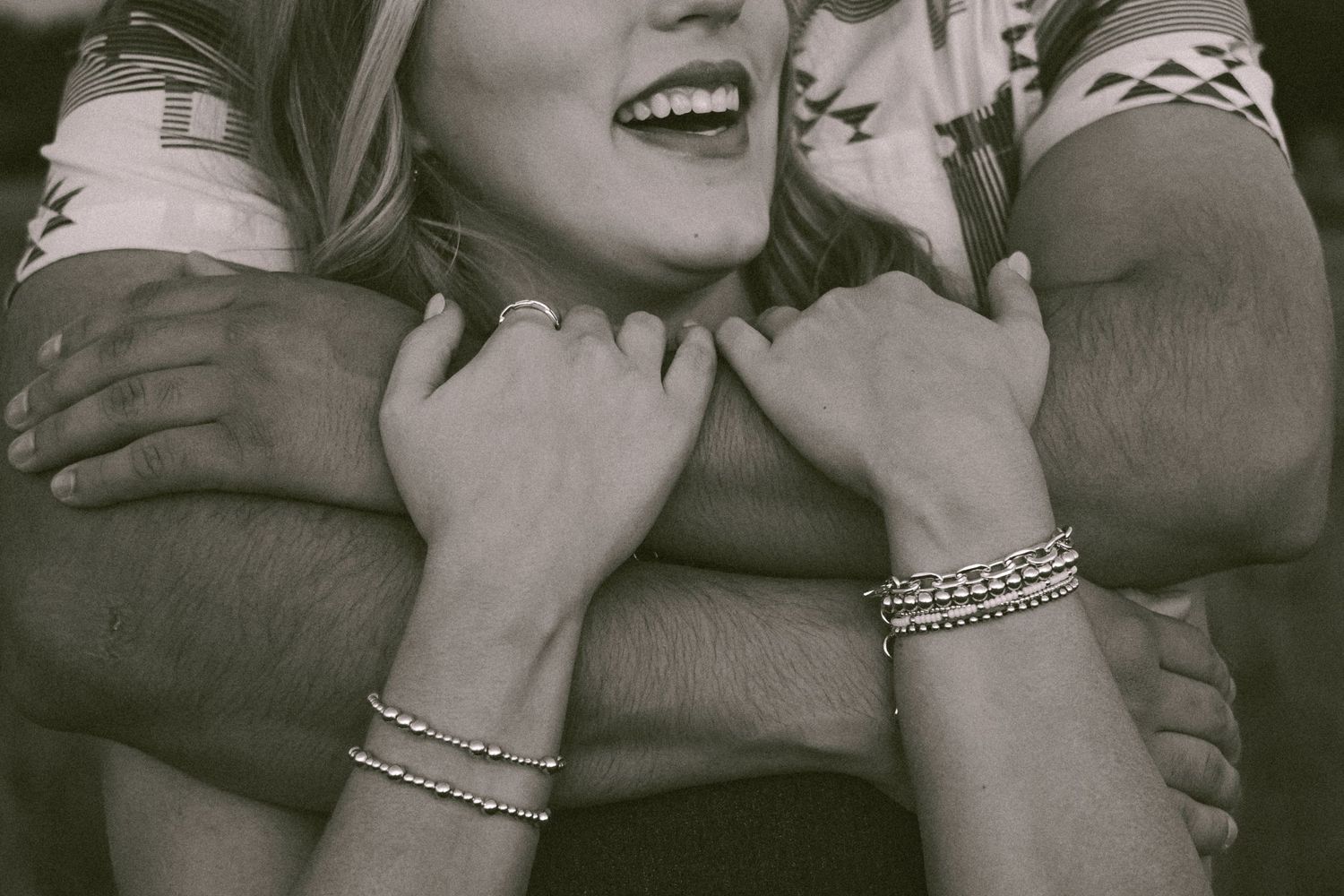 Close-up black and white photo showing hands embracing someone wearing bracelets while sharing a joyful moment.